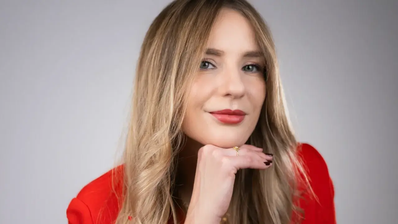 Francesca Florio, con un blazer rosso, appoggia il mento sulla mano, un sorriso pensieroso.