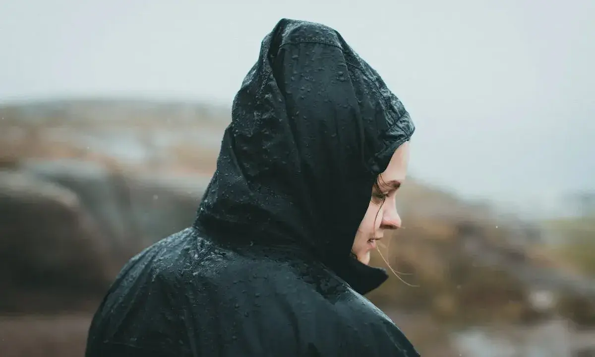 Person i regnkläder med huvan uppdragen, droppar på tyget. Vattenpelare 10000 klarar detta väder.