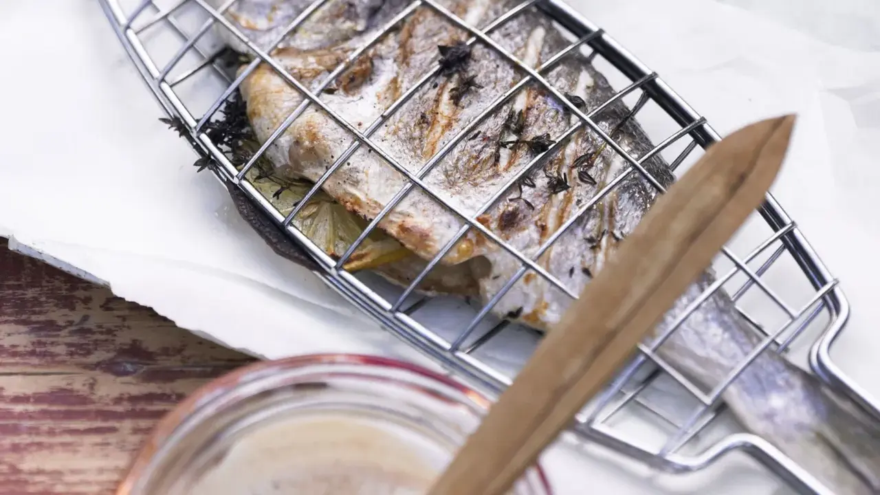 Ein ganzer Fisch liegt in einem Grillkorb, bereit zum Fisch grillen auf dem Elektrogrill. Kräuter und Zitronenscheiben sind im Fisch.