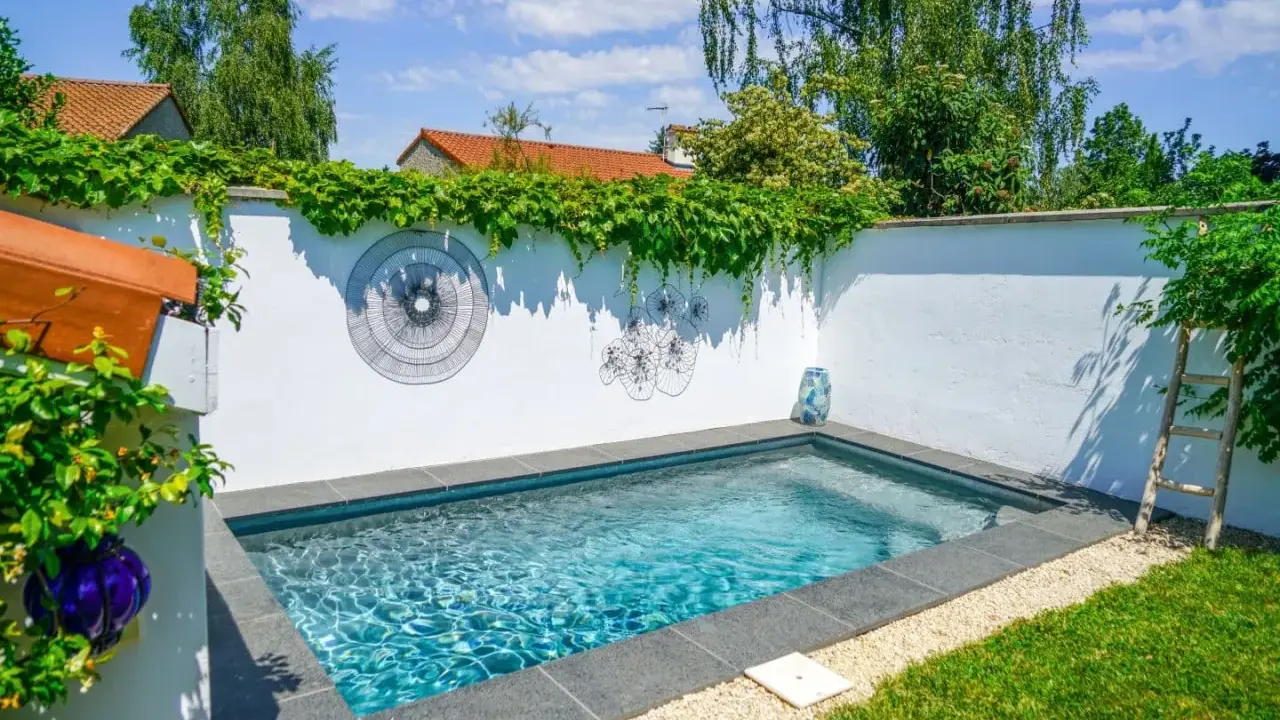 Petite piscine bleue dans un jardin verdoyant, décorée d'art mural. Un projet de permis de construire piscine réussi.