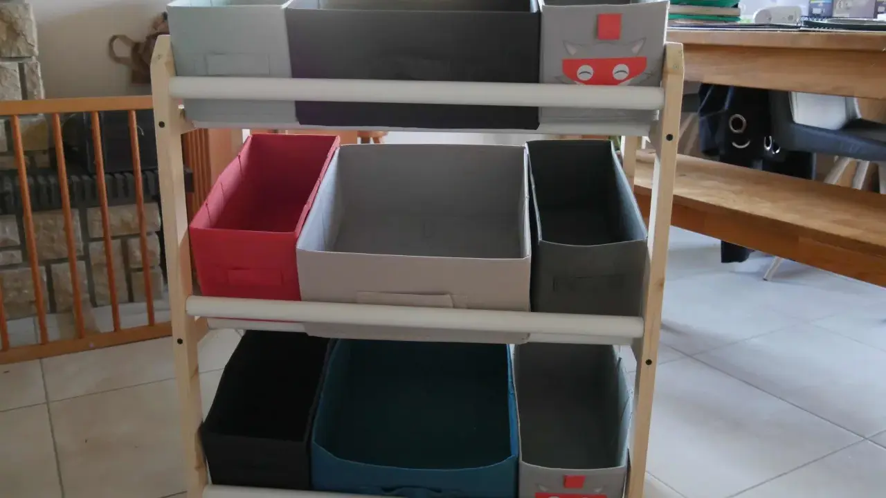 Étagère en bois avec des bacs de rangement pour jouets, dont un décoré d'un chat super-héros. Idéal pour fabriquer un rangement jouet organisé.