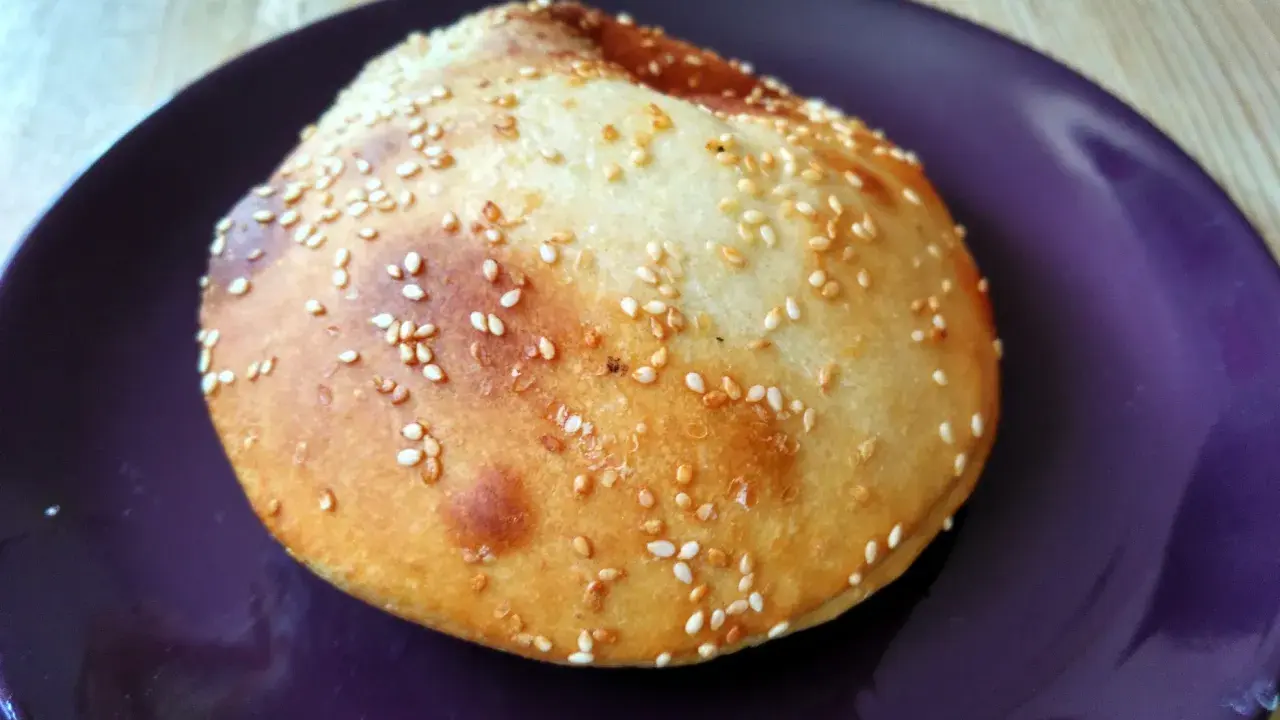 Bułka do hamburgerów posypana sezamem na fioletowym talerzu.