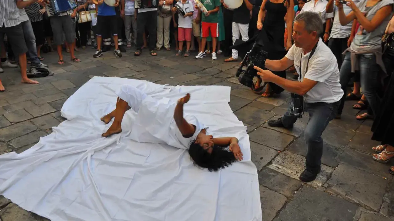 Danza contemporanea durante la festa patronale Galatina. Un performer si muove su un telo bianco, ripreso da un operatore.