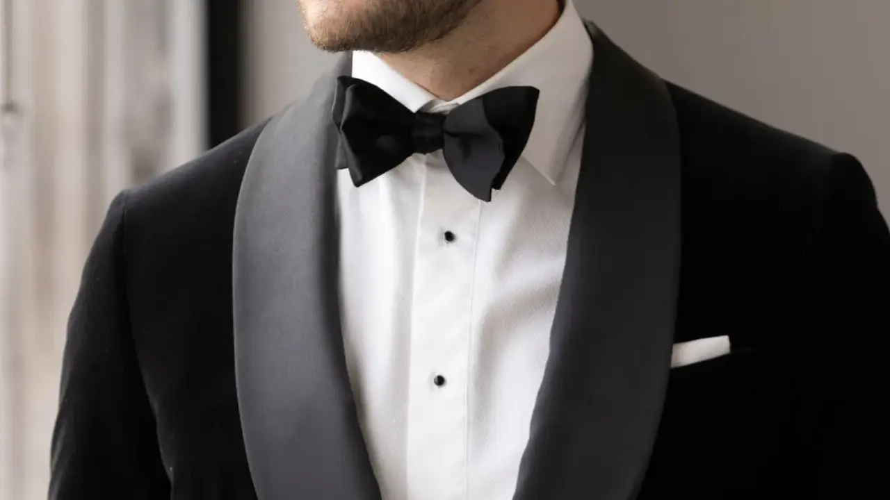 A man wears a sharp black suit with a crisp white shirt and a black bow tie, ready for a formal occasion.