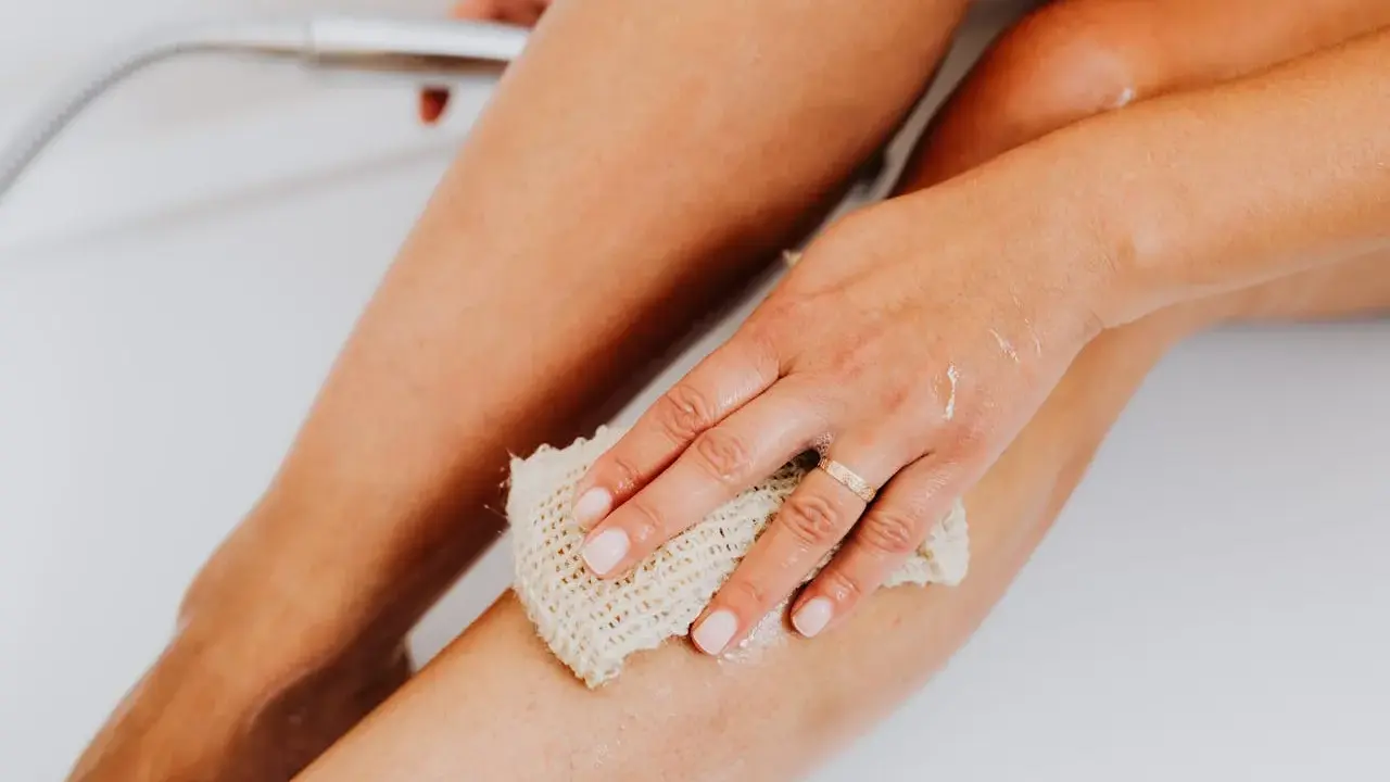 Une main utilise un gant de toilette pour exfolier sa peau, révélant une peau douce et lisse. C'est une étape clé pour savoir comment exfolier sa peau.
