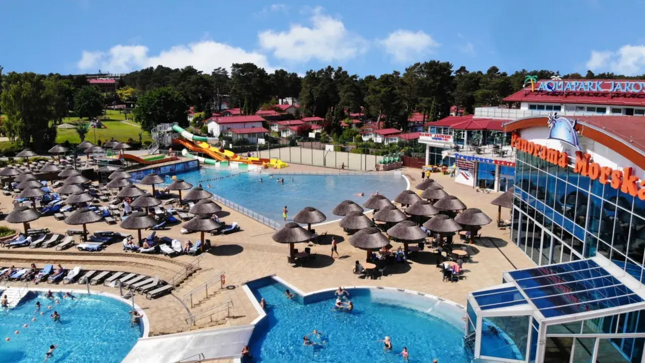 Słoneczny aquapark nad morzem z basenami, zjeżdżalniami i leżakami pod parasolami.