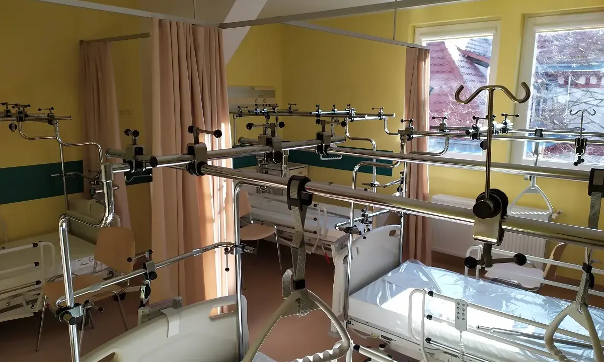Szpitalna sala z łóżkami i aparaturą ortopedyczną.