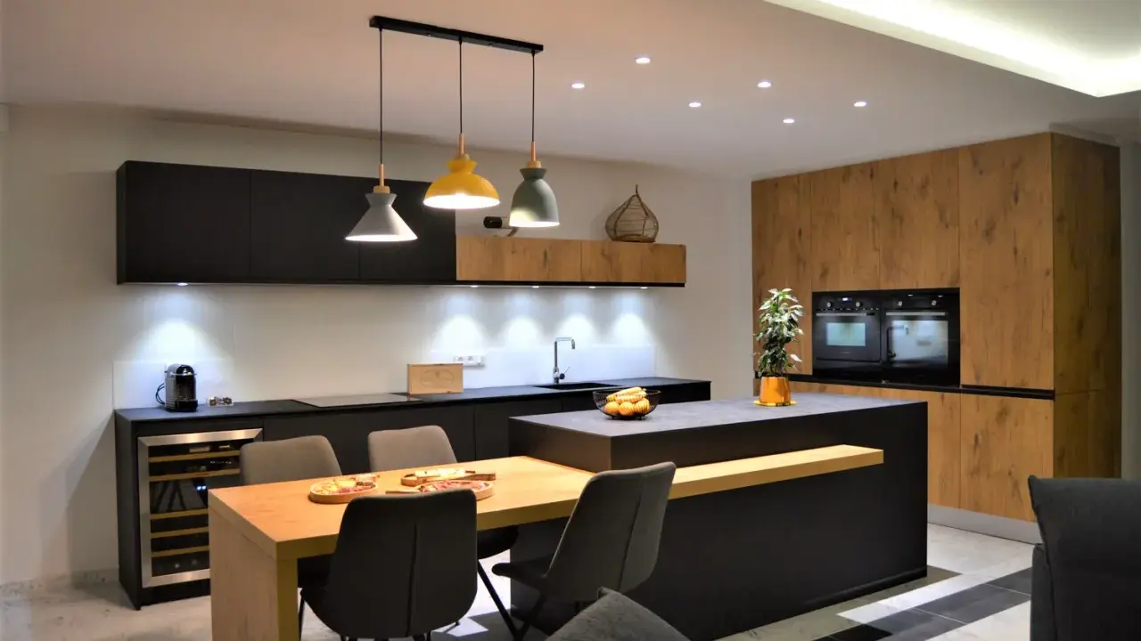 Une cuisine moderne aux accents beige et noir, avec un îlot central, des meubles en bois et des suspensions colorées.
