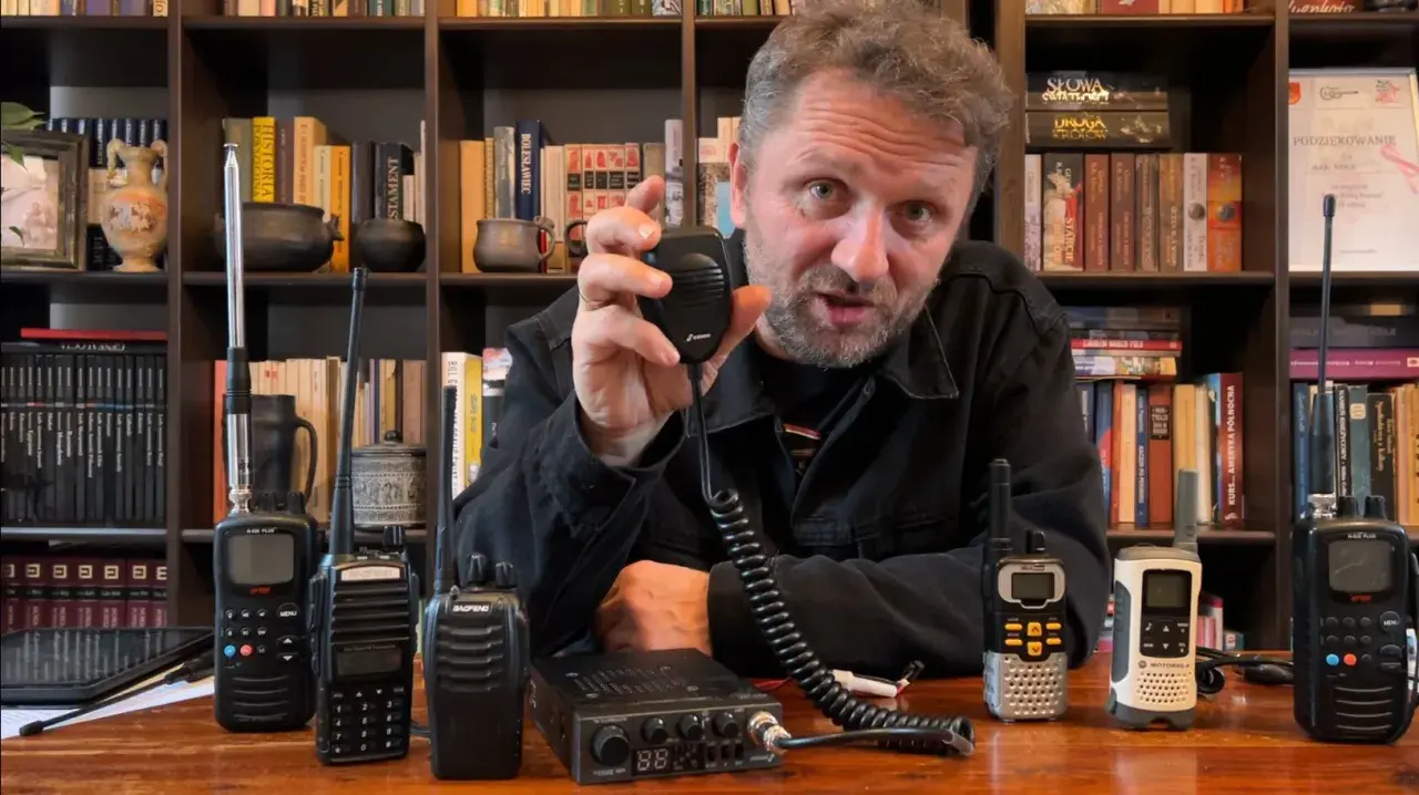 Mężczyzna prezentuje sprzęt CB radio, pokazując różne modele i akcesoria, które wpływają na zasięg.