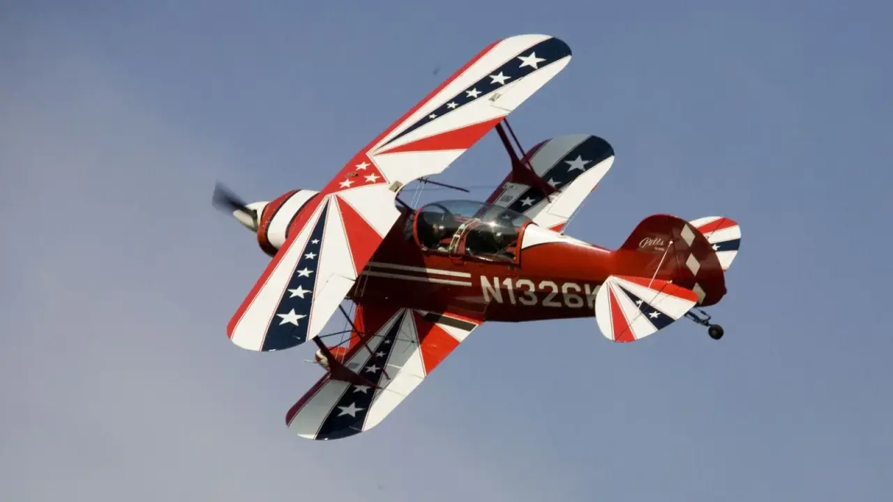 Rotes Pitts Special Doppeldeckerflugzeug mit Sternenmuster fliegt im blauen Himmel.