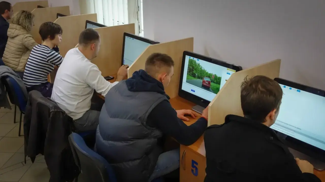 Ludzie siedzą przy komputerach, rozwiązując testy. Tak sprawdzisz, jak zdałeś egzamin teoretyczny na prawo jazdy.