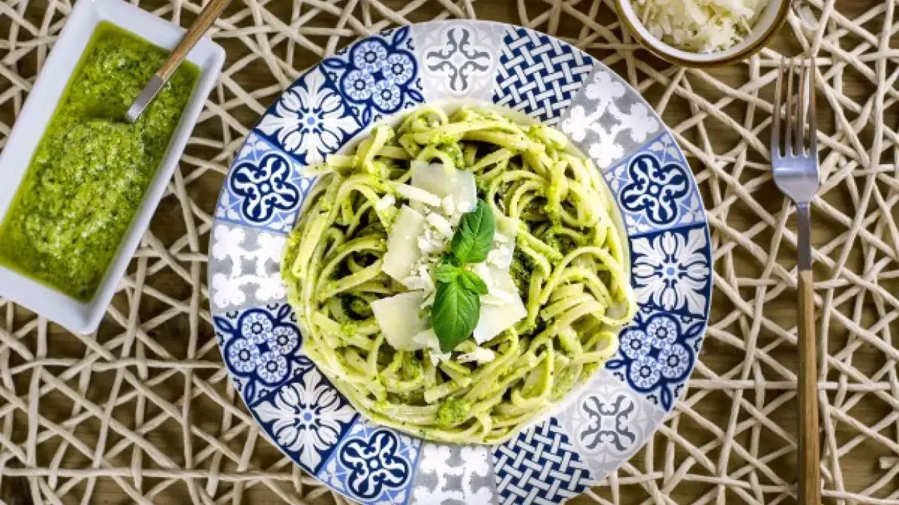 Deliciosa pasta con pesto, ideal para tus recetas de pasta con pesto. Servida en un plato decorado con un toque mediterráneo.