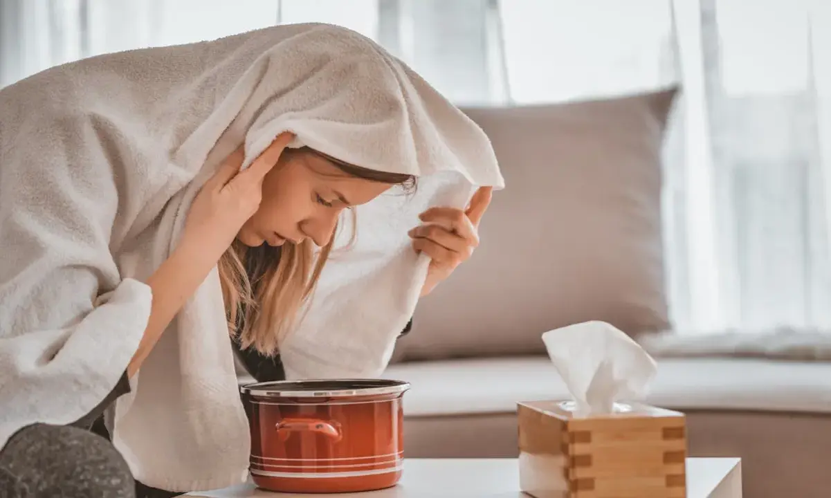 Une femme apprend comment faire une inhalation, la tête couverte d'une serviette au-dessus d'une casserole de vapeur.