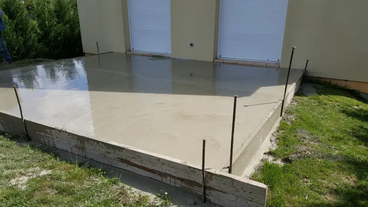 Une nouvelle dalle béton fraîchement coulée, prête à sécher. Les coffrages en bois et les fers à béton délimitent la zone.