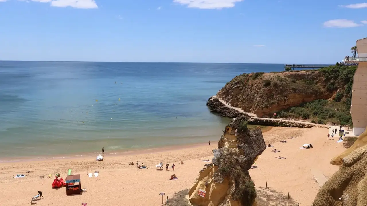 Sonniger Lagos Strand mit goldenem Sand, türkisfarbenem Wasser und Felsformationen. Menschen entspannen sich, spielen und genießen die Aussicht.
