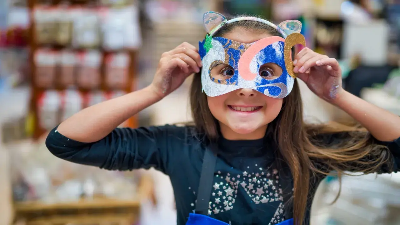 Une jeune fille, le visage caché par un masque coloré, explore la symbolique du visage et la joie de la transformation.