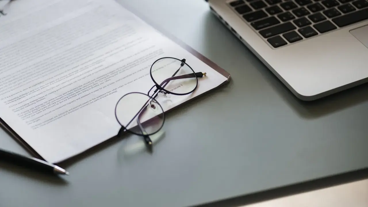 Okulary na dokumencie z tekstem, obok laptopa. Dokument może zawierać pełnomocnictwo lub strategię marketingową.