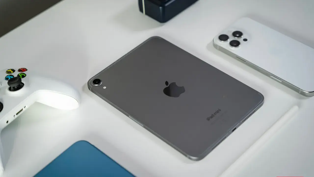 Szary iPad mini, biały kontroler do gier, biały iPhone i rysik na białym tle.