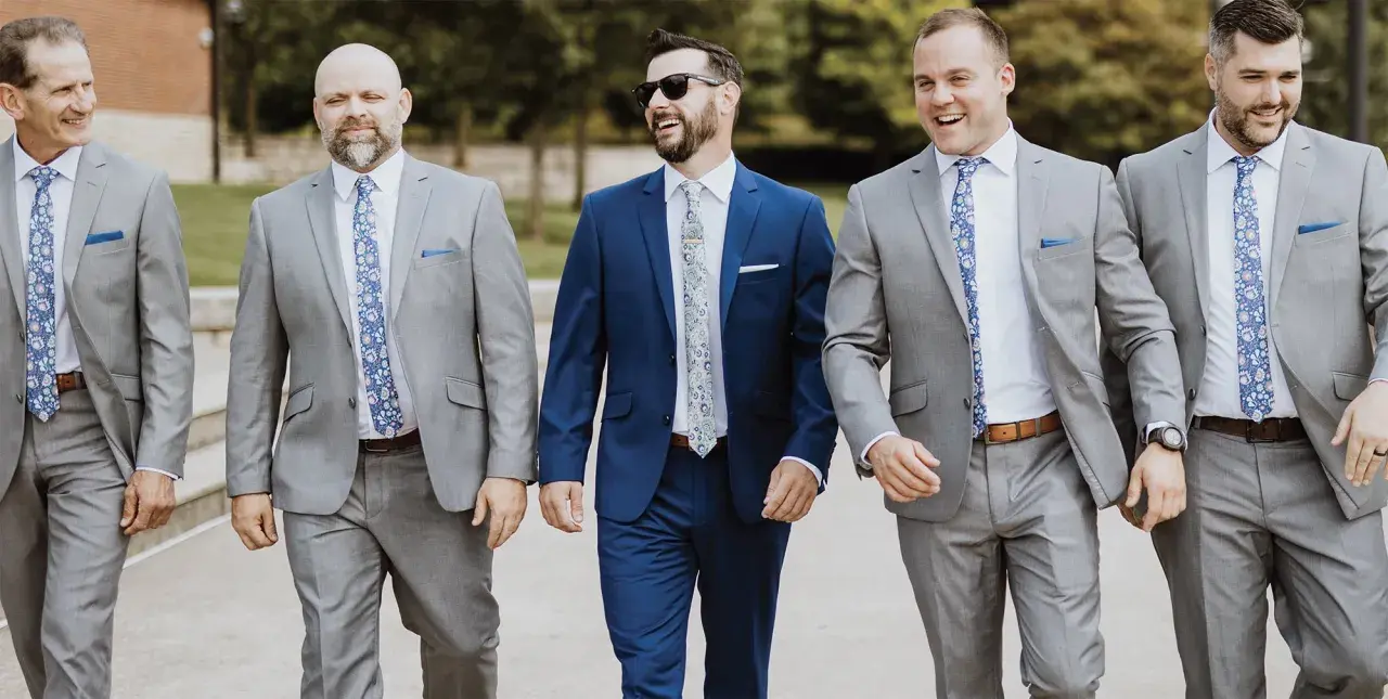 Groomsmen in grey suits and patterned ties walk together, showcasing stylish wedding pocket square folds.