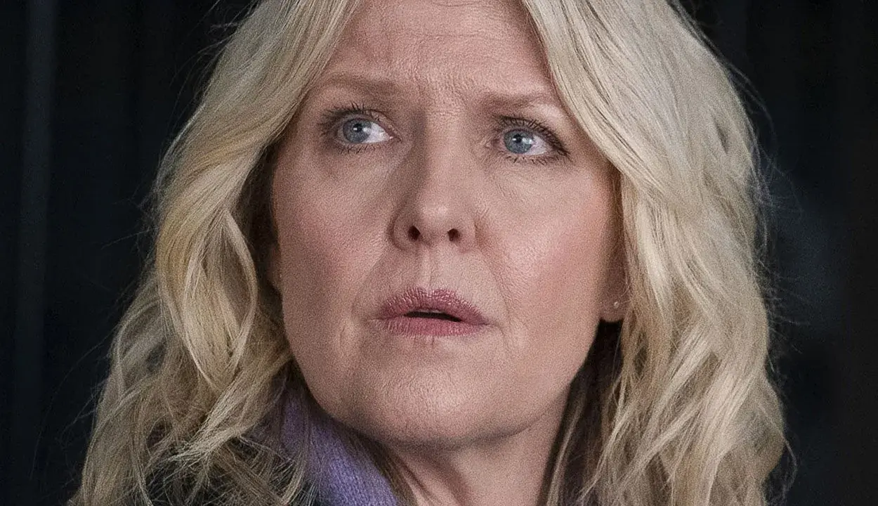 En kvinna med blont hår och blå ögon, klädd i lila, ser oroligt ut. Kanske är hon mitt i ett dramatiskt ögonblick i **shetland serie**.