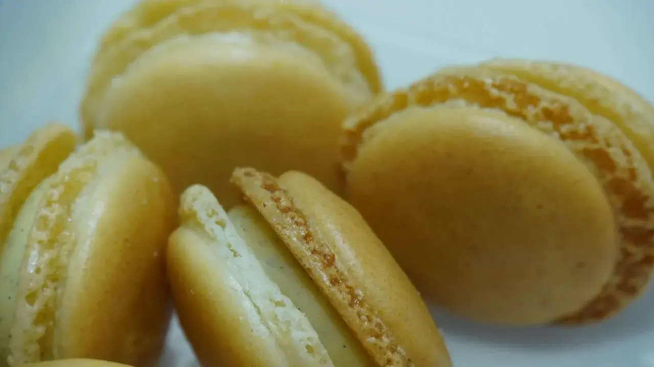 Macarons dorés à la ganache vanille, leurs coques délicates révèlent une garniture crémeuse et parfumée.