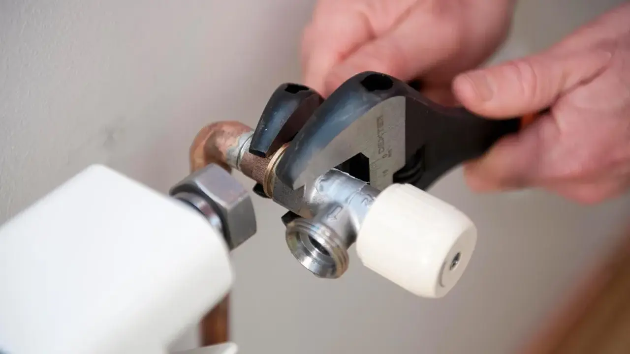 Manos ajustando llave de radiador con llave inglesa para cambiarla y evitar goteos.
