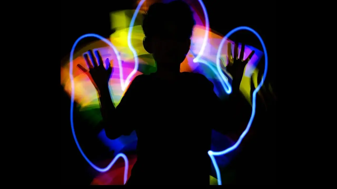 Silueta de niño jugando con light painting, creando auras de colores vibrantes a su alrededor.