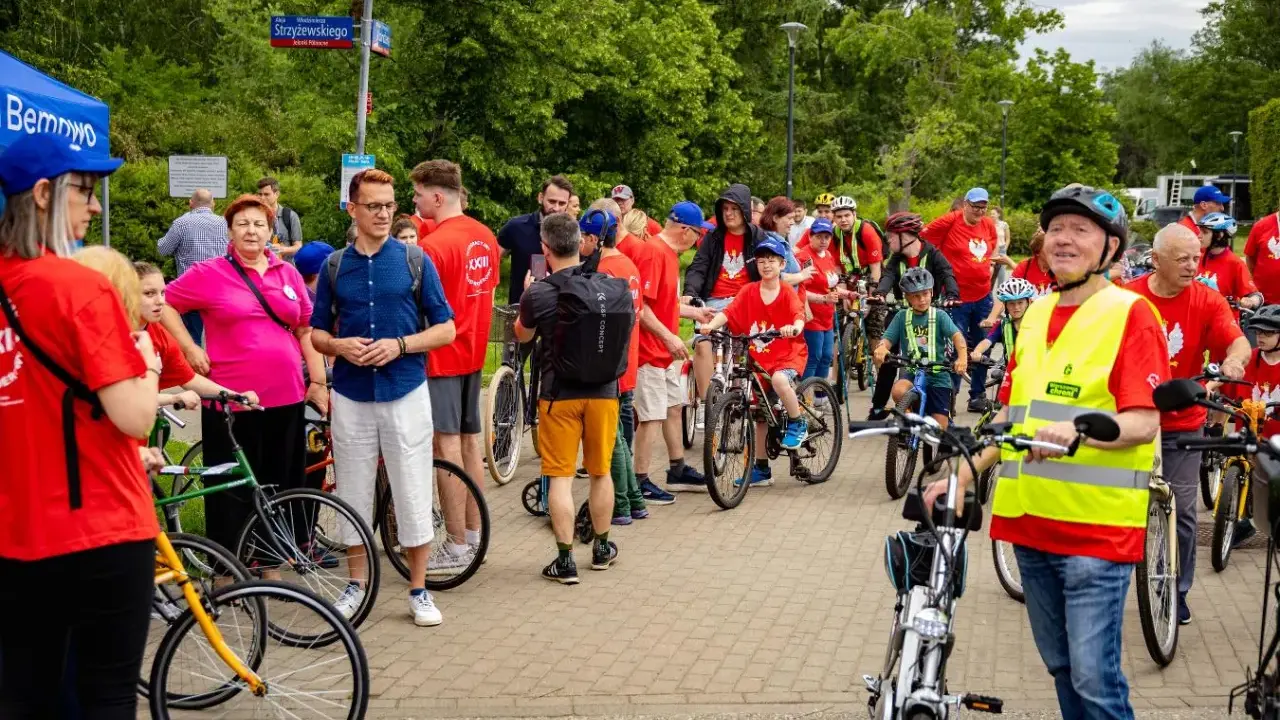 Uczestnicy rajdu rowerowego w czerwonych koszulkach, dzieci i dorośli, gotowi do startu.
