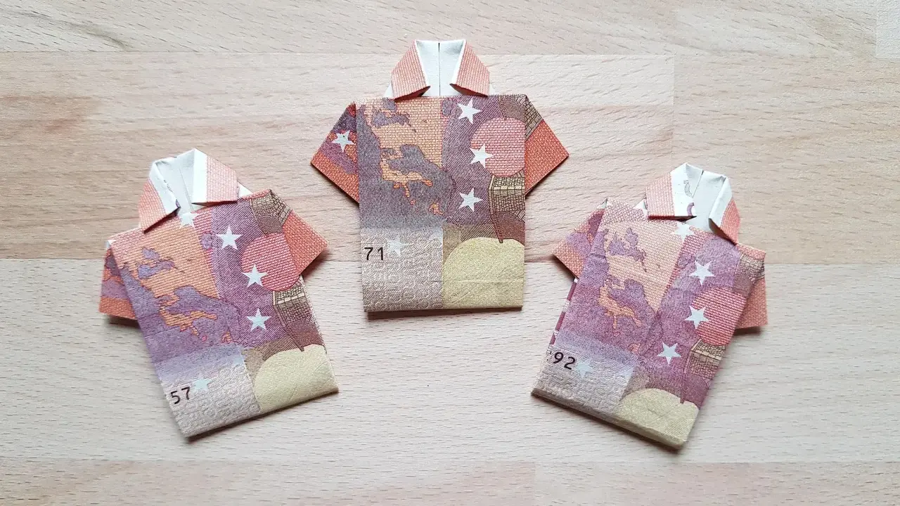Drei gefaltete Euro-Scheine in Form von Hemden liegen auf einem Holztisch. Das kunstvolle Falten von Geld zu kleinen Hemden ist eine kreative Idee.