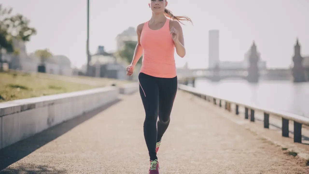 Frau joggt am Fluss entlang. Sie beweist, dass ist joggen gesund und ein toller Start in den Tag.