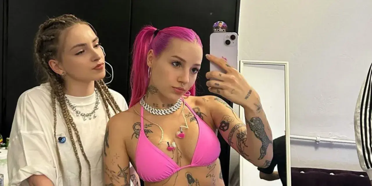 Dwie młode kobiety, jedna z różowymi włosami i tatuażami, druga z warkoczami, pozują do selfie.