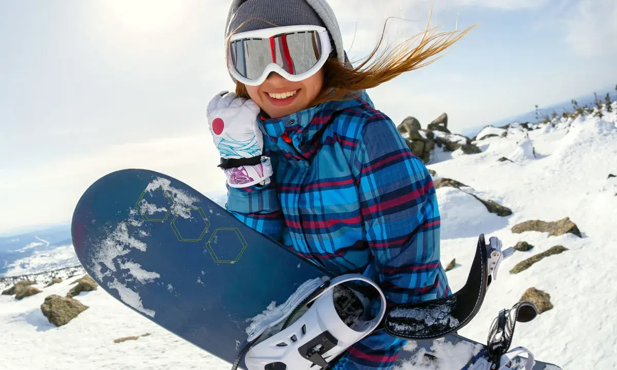 Uśmiechnięta snowboardzistka z deską, idealny dobór deski snowboardowej do wzrostu i wagi to klucz do zabawy na stoku.