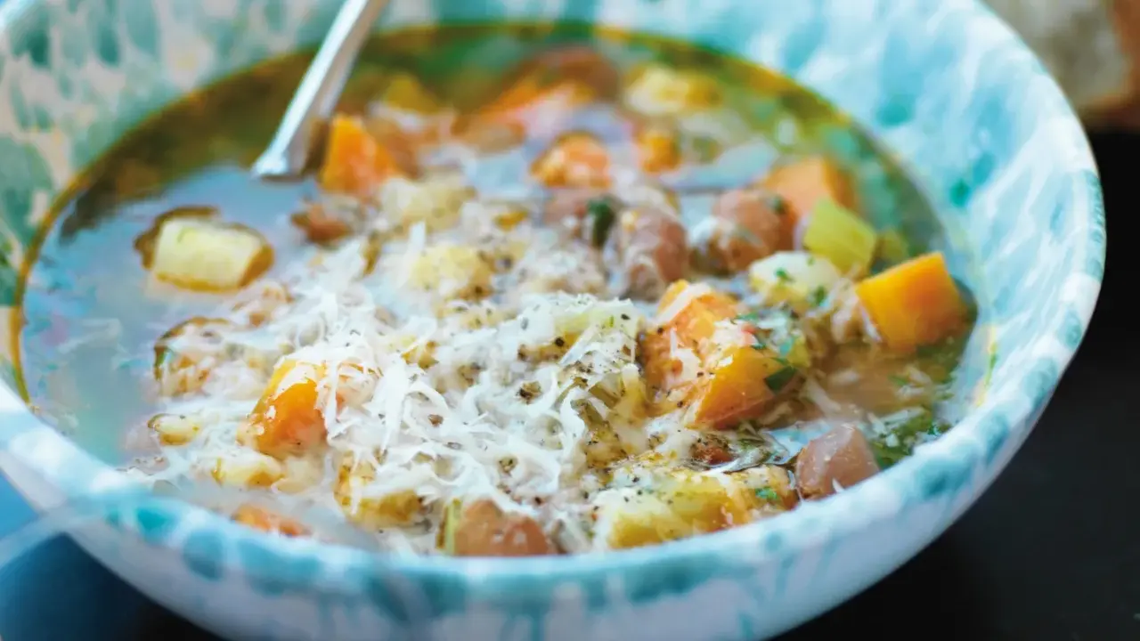 En närbild av en skål med mustig rotfruktssoppa, toppad med riven ost. Ett perfekt soppa recept för kalla dagar.