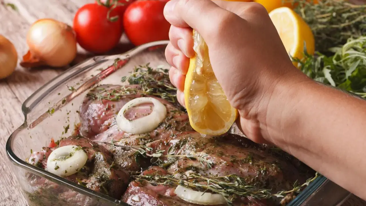 Fleisch marinieren für den Grill: Zitrone über mariniertes Fleisch mit Zwiebeln und Kräutern ausdrücken.