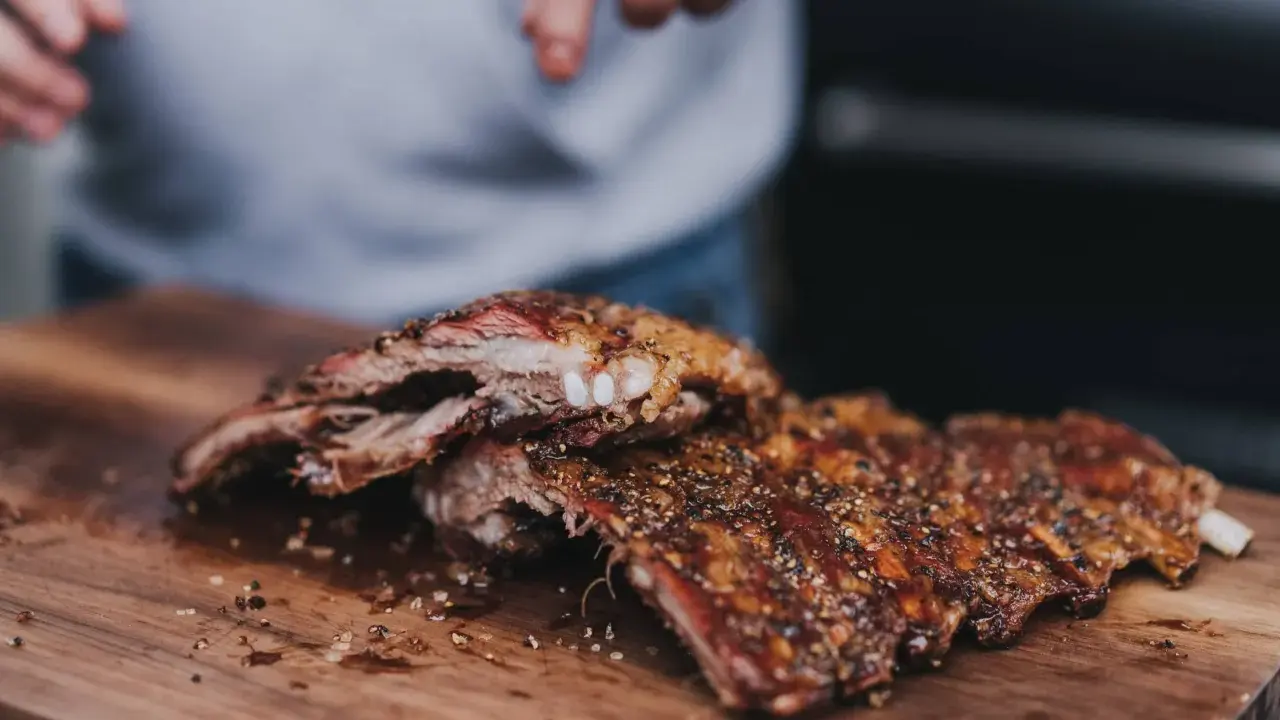 Saftige, gewürzte 321 Ribs liegen auf einem Holzbrett. Hände im Hintergrund bereiten sie für den Genuss vor.