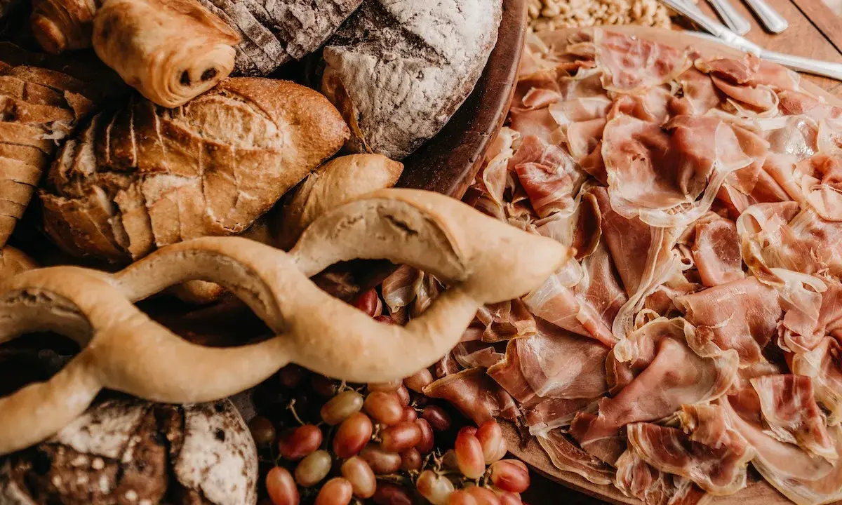 Un assortiment de pains artisanaux, de jambon cru et de raisins, parfait pour un pain sandwich italien gourmand.