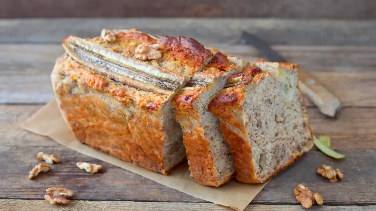 Pyszny chlebek bananowy z bakaliami, pokrojony w kromki, z widocznymi orzechami i bananem na wierzchu.