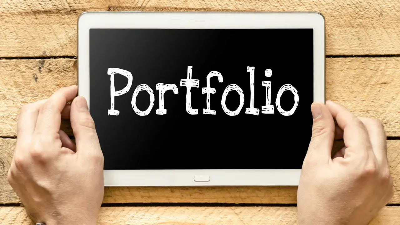 Ręce trzymają tablet z napisem "Portfolio". Idealny do prezentacji prac podczas studiów.