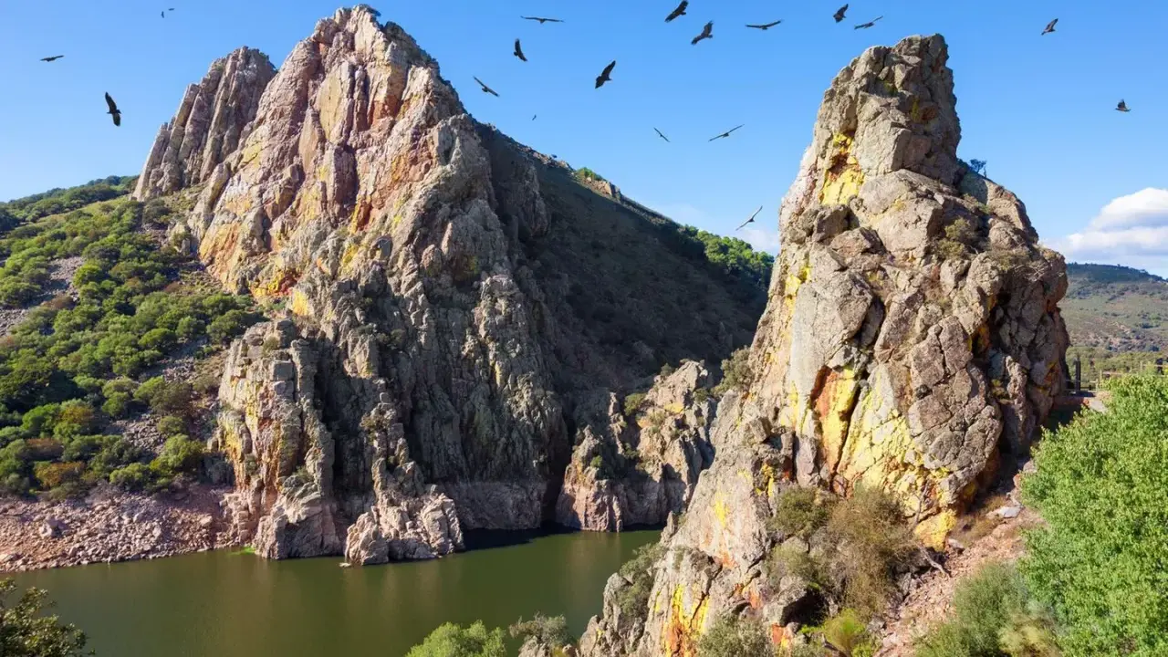 Felsige Berge und ein Fluss in Extremadura, Spanien. Geier kreisen am blauen Himmel über der rauen Landschaft.