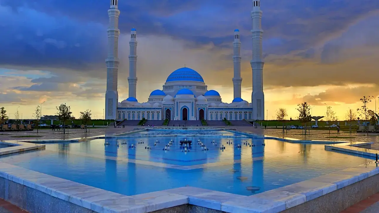 Die Hazrat-Sultan-Moschee in Astana, ein architektonisches Meisterwerk, spiegelt sich im Wasser eines Brunnens unter einem dramatischen Abendhimmel.