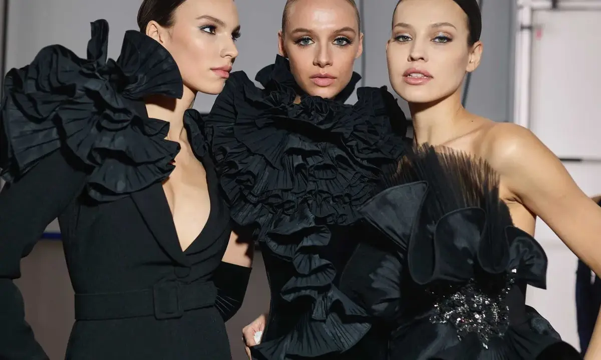 Tres modelos lucen peinados recogidos elegantes, perfectos para una fiesta, con vestidos negros voluminosos y detalles de volantes.