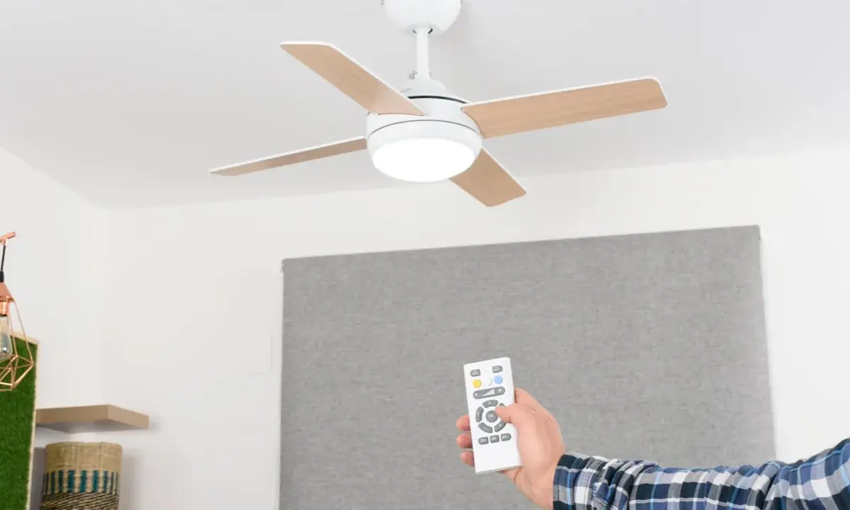 Mano con mando a distancia operando un ventilador de techo escayola con luz integrada.