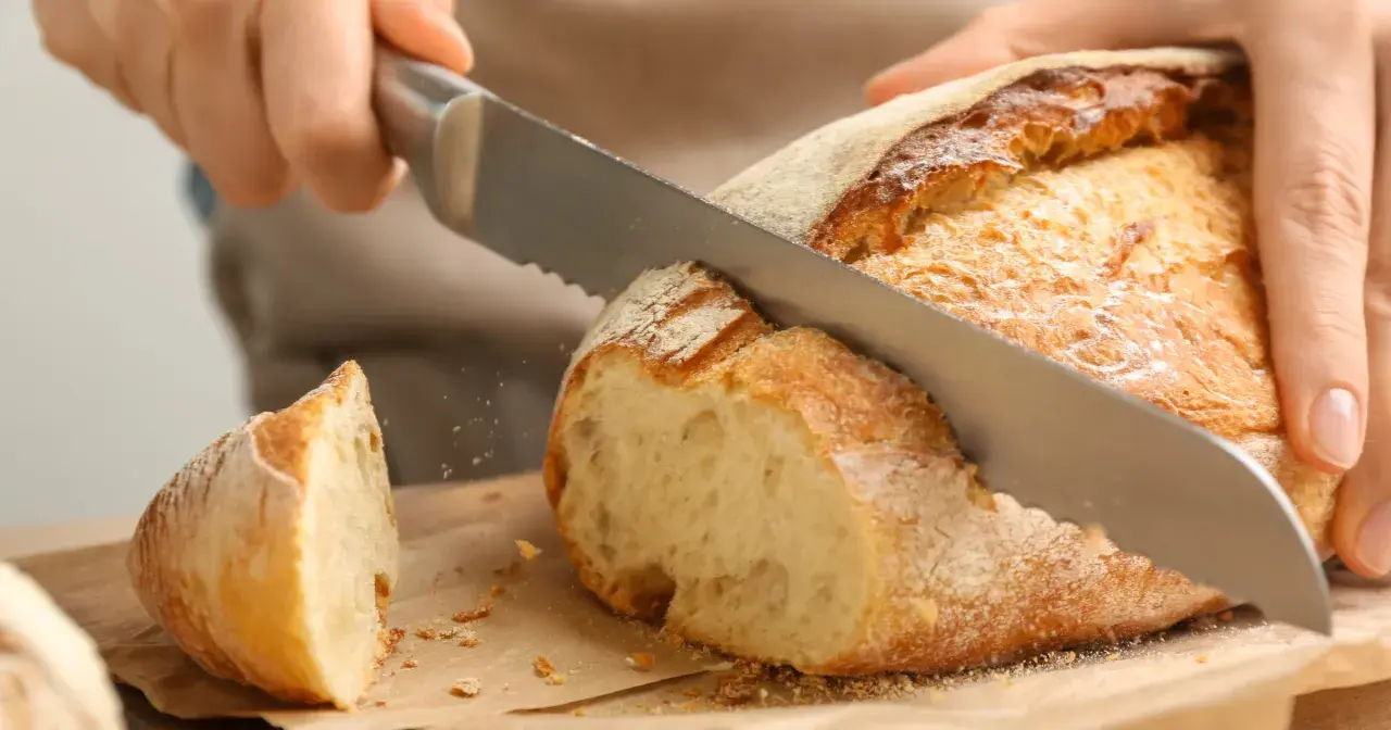 Krojenie świeżo upieczonego bochenka, idealnego na domowy przepis na chleb pieczony w piekarniku. Chrupiąca skórka i miękki środek.