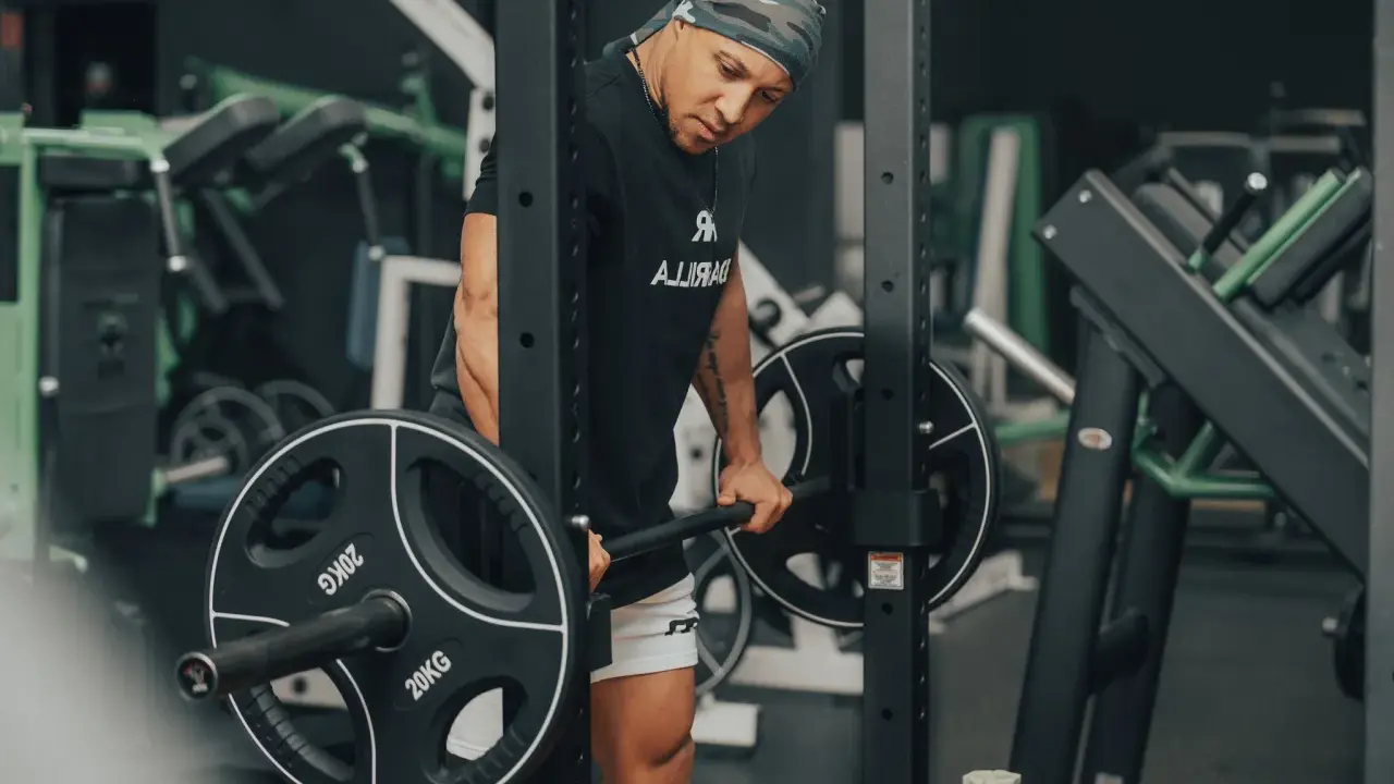 Mann im Fitnessstudio bereitet sich auf schwere myo reps vor, hält eine Langhantel mit 20kg Scheiben.