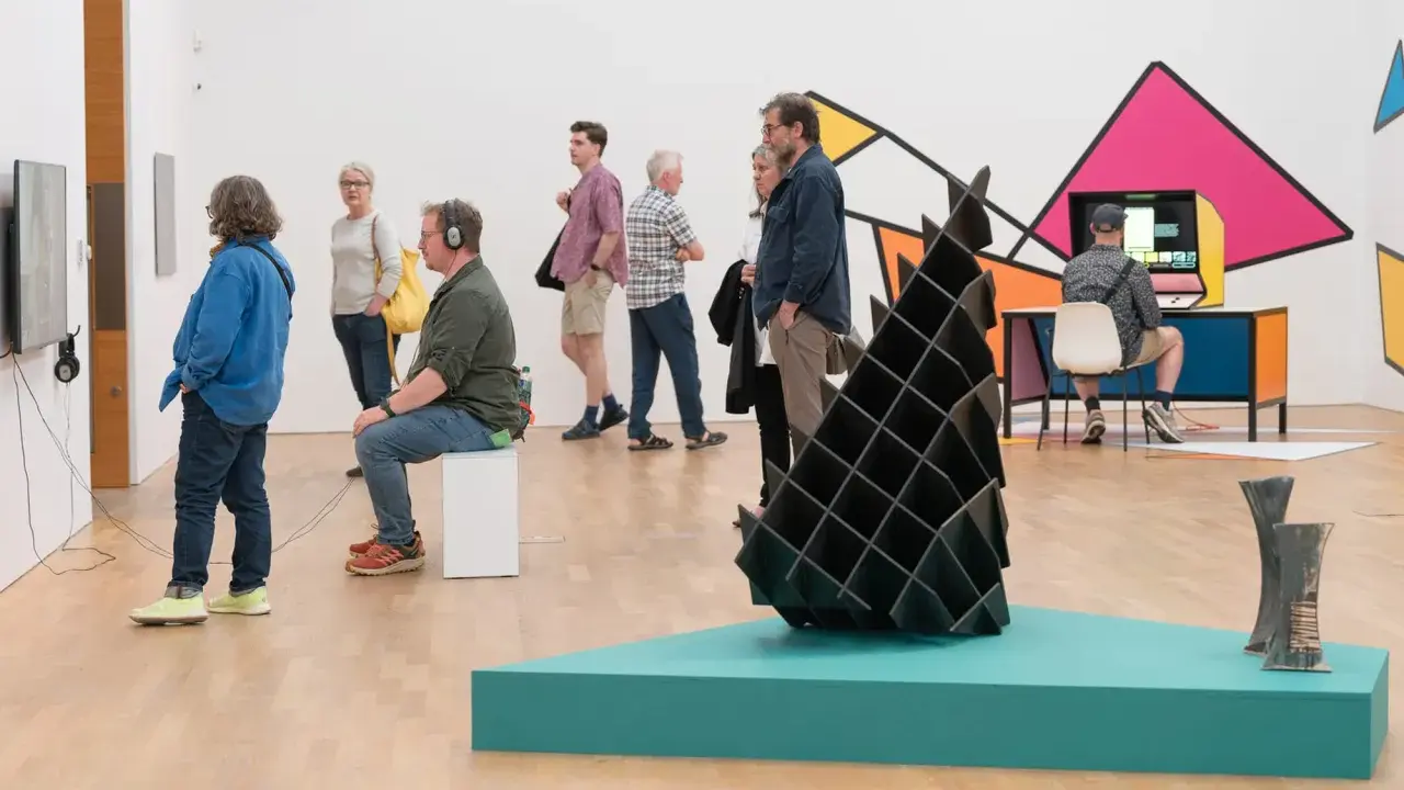Visitors explore diverse artworks in what is an art gallery, from video installations to abstract sculptures and colorful wall art.