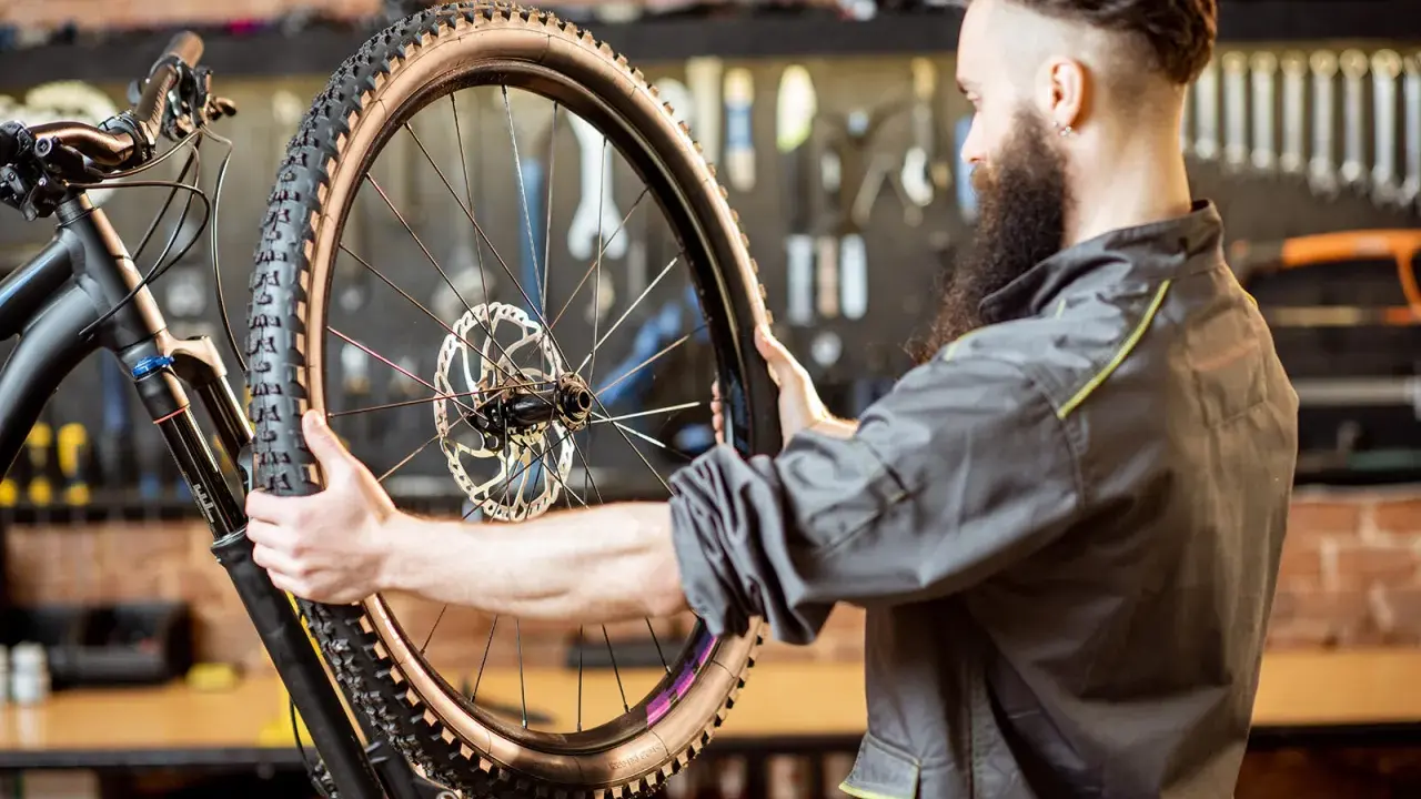 Mechanik z brodą sprawdza oponę gravelową roweru. Zastanawia się, ile mleka do opony gravel będzie potrzebne, by zapewnić najlepszą przyczepność.