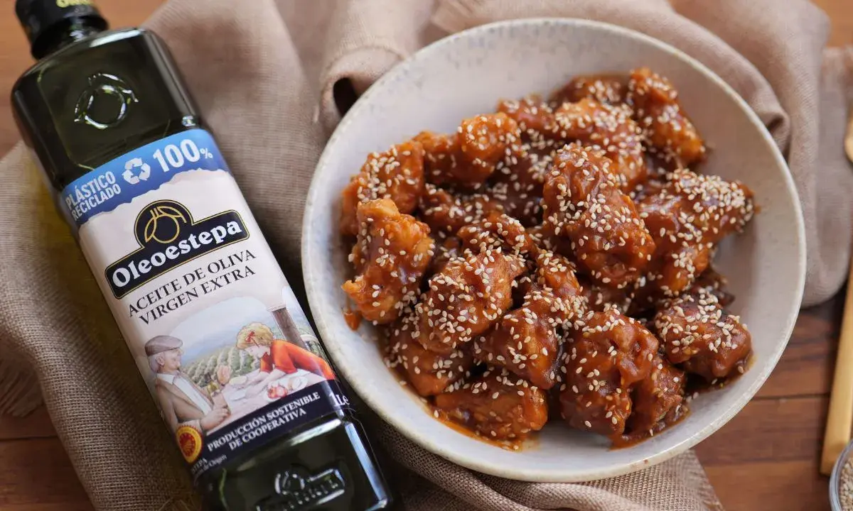 Delicioso pollo agridulce cubierto de semillas de sésamo en un cuenco, junto a una botella de aceite de oliva virgen extra Oleoestepa.