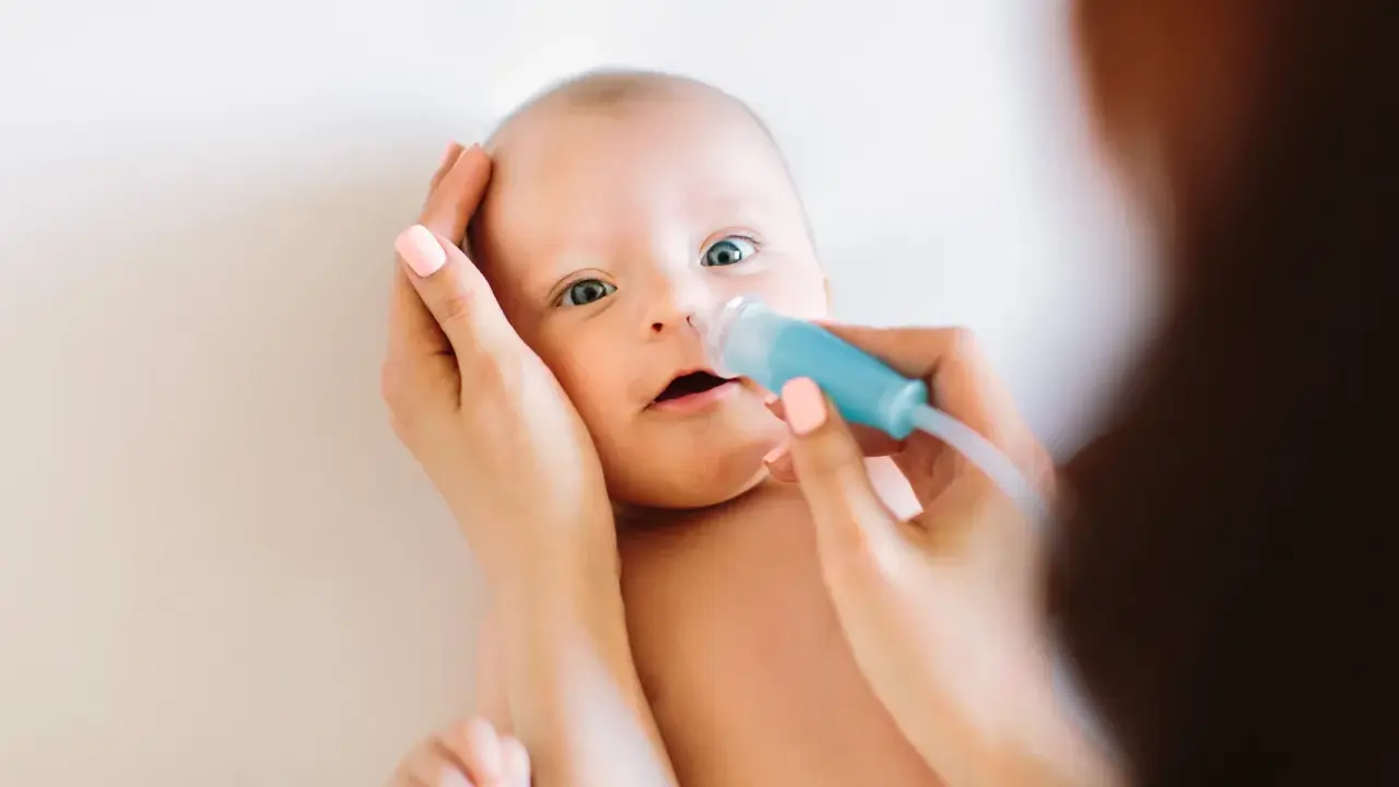 Mama delikatnie oczyszcza nosek niemowlaka z katarem za pomocą aspiratora.