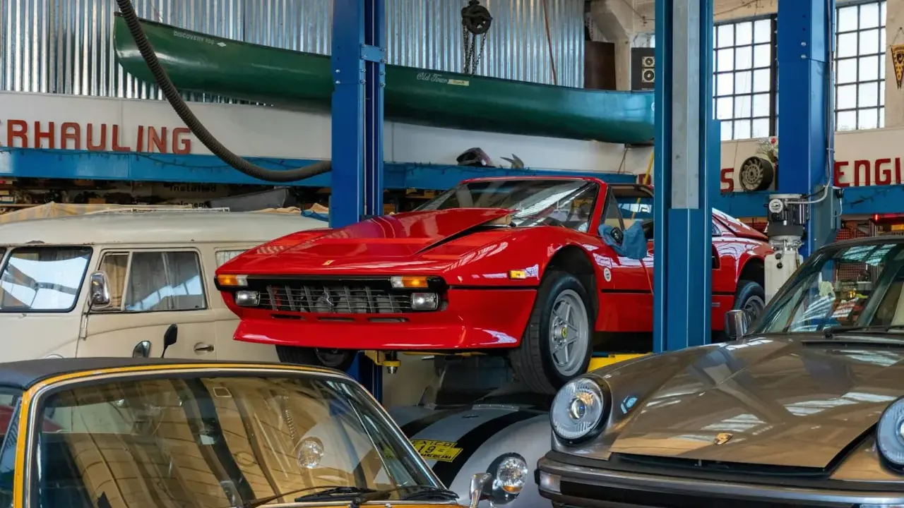 Taller mecánico con autos clásicos: un rojo Ferrari en elevador, un Porsche gris y un amarillo. ¡Ideas para tu taller!
