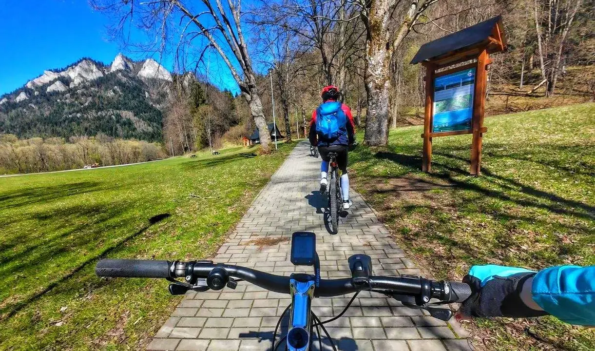 Rowerzyści przemierzają malowniczą ścieżkę rowerową w Szczawnicy, podziwiając górskie krajobrazy.